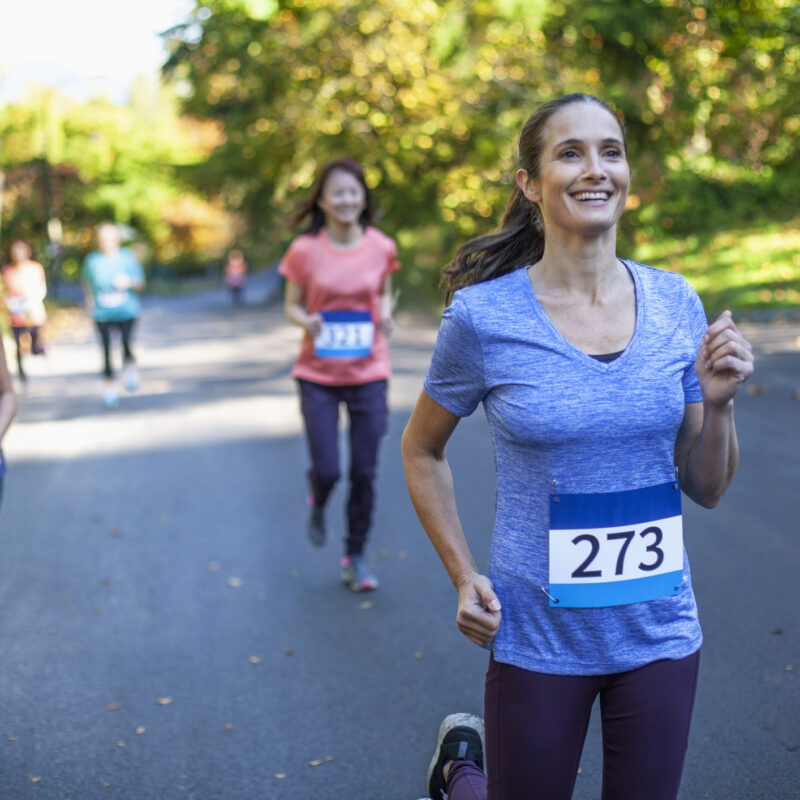 Mature multiracial woman runs in marathon race with group of women in park
